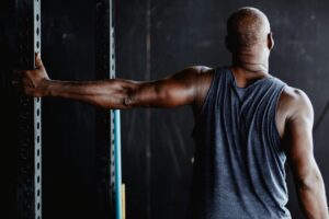 Athlete reaching one arm overhead against a squat rack, demonstrating overhead shoulder mobility